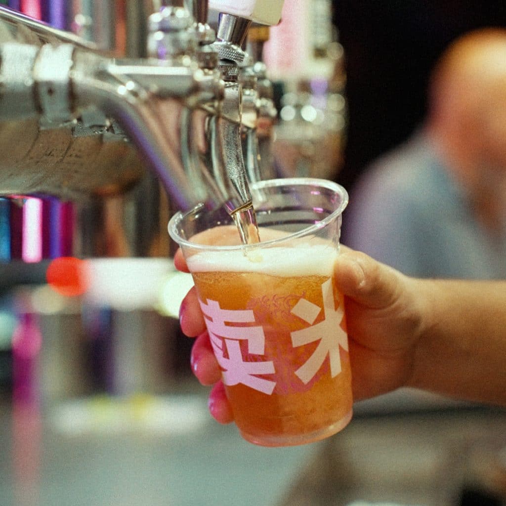Hand holding a Rice Box branded cup as golden craft beer pours from a tap